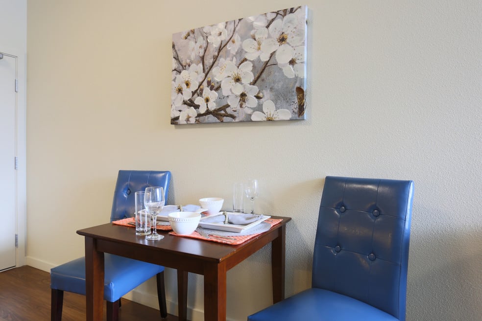 Cozy dining area with blue chairs and a floral painting.