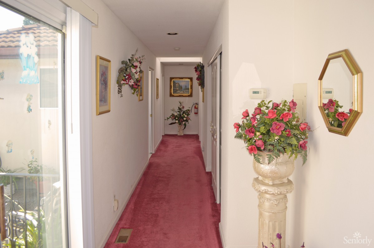 A carpeted hallway adorned with floral arrangements and paintings.