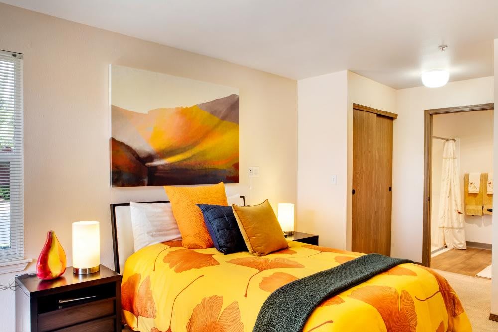 A cozy bedroom with vibrant orange and yellow bedding, complemented by abstract wall art and soft lighting.