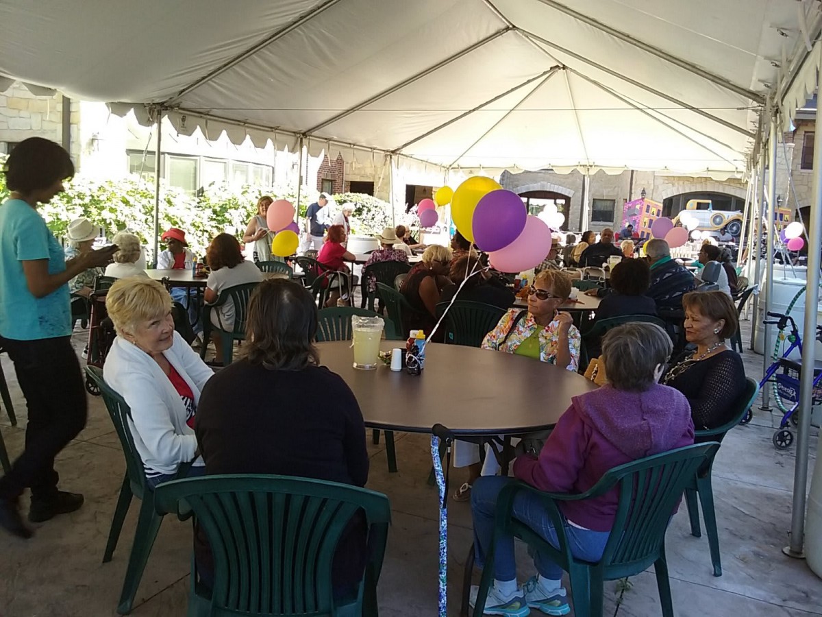 A lively outdoor gathering under a tent, decorated with colorful balloons and filled with people enjoying the event.