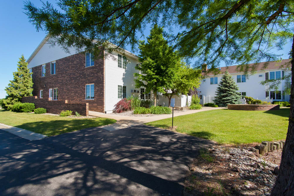 A sunny day view of a residential apartment building surrounded by trees and a grassy area.