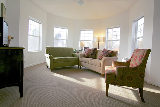 A bright living room with sofas and armchairs arranged near large windows.
