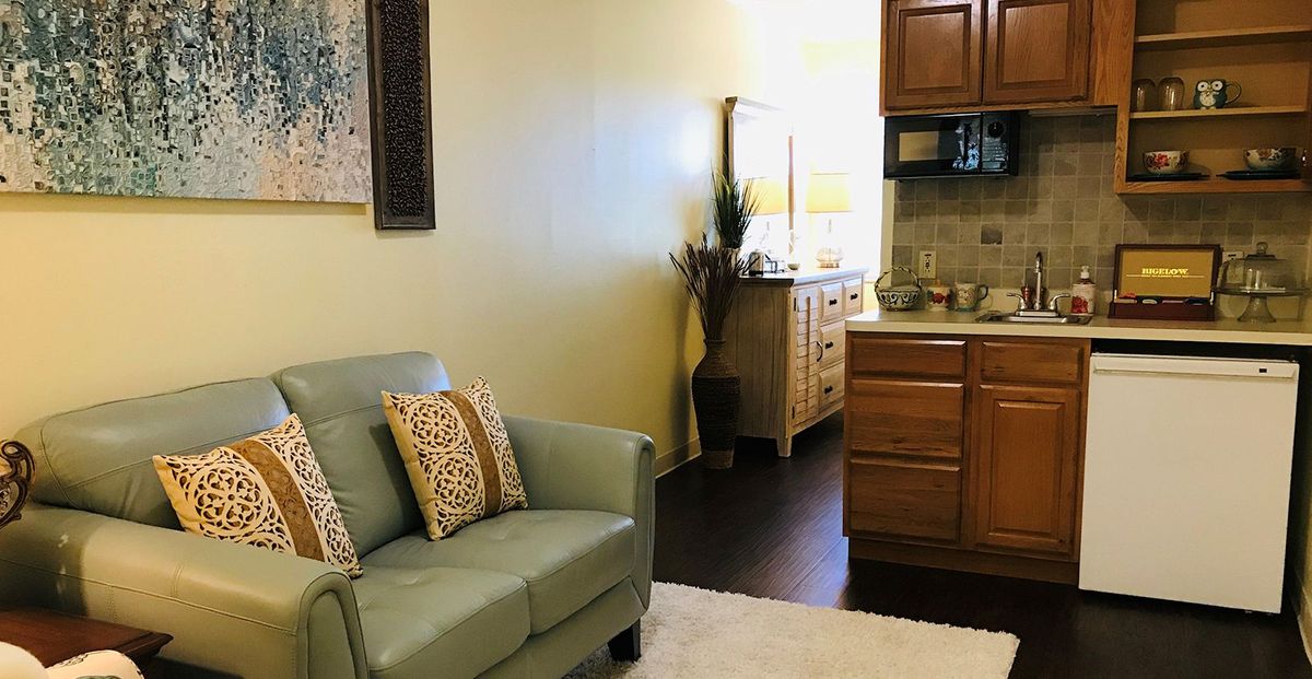 A cozy living room with a green sofa and a view of the kitchen area featuring wooden cabinets.