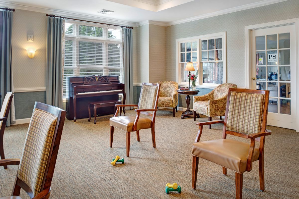 A cozy living room with a piano, several chairs, and large windows allowing natural light.