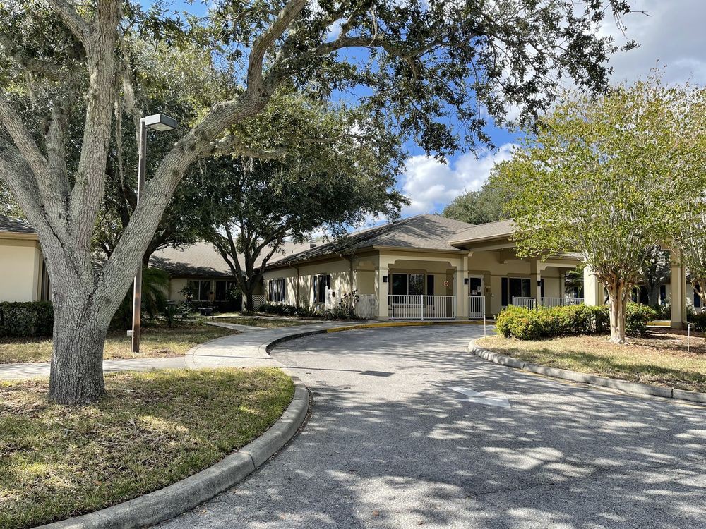 A view of a building with surrounding trees and a curved driveway under a partly cloudy sky.