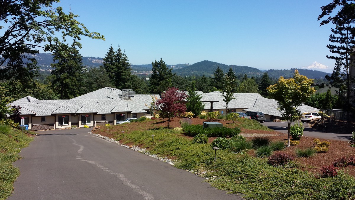 A scenic view of a building surrounded by trees and mountains under a clear blue sky.