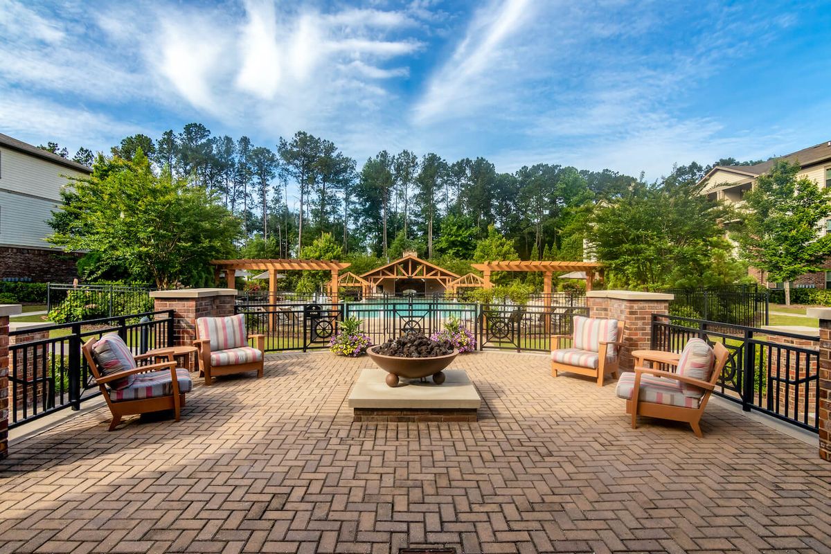 A beautiful outdoor patio with comfortable seating, a central fire pit, and a pergola overlooking a lush garden.