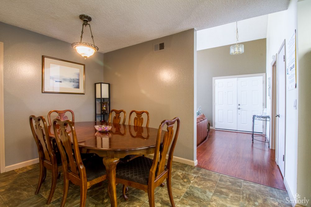 A cozy dining room features a wooden table with chairs, adorned by a chandelier and complemented by floor tiles.