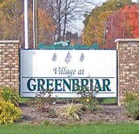 Entrance sign for the Village at Greenbriar with brick pillars and autumn foliage.