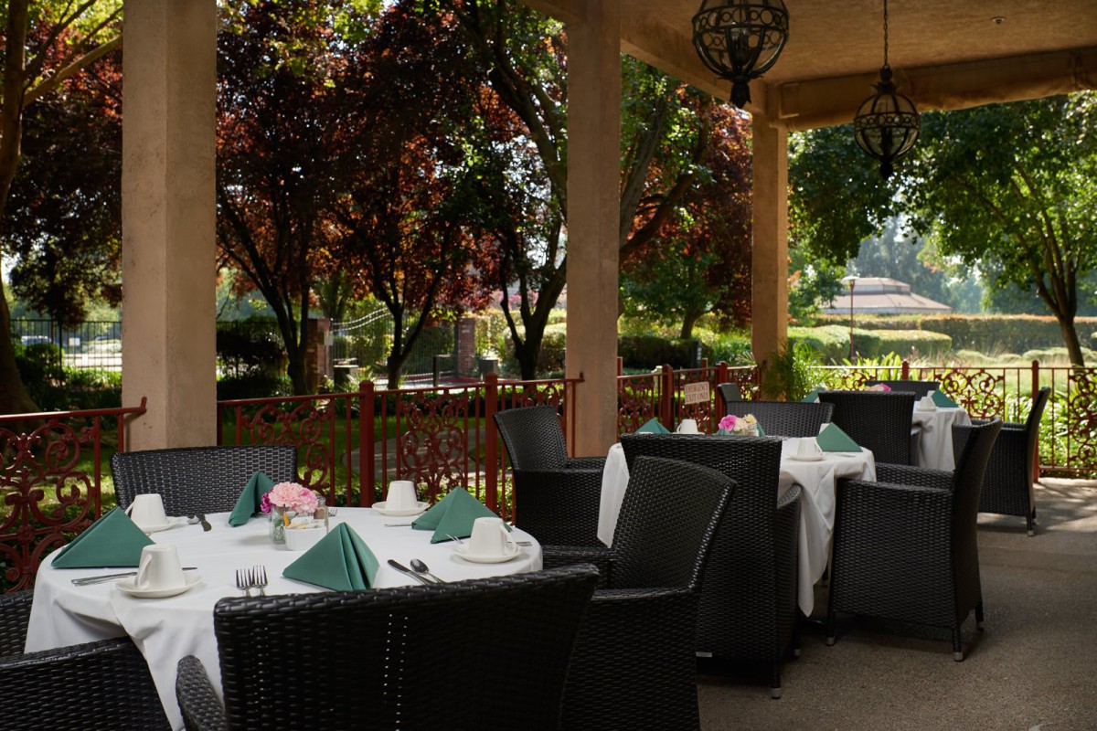 An inviting outdoor dining area with neatly set tables surrounded by lush greenery.