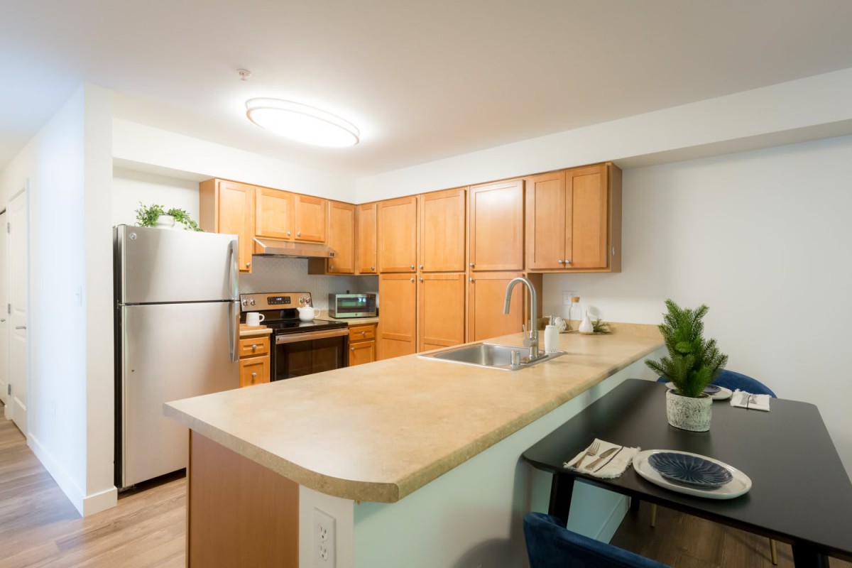 A modern kitchen with wooden cabinets, stainless steel appliances, and a cozy dining area.