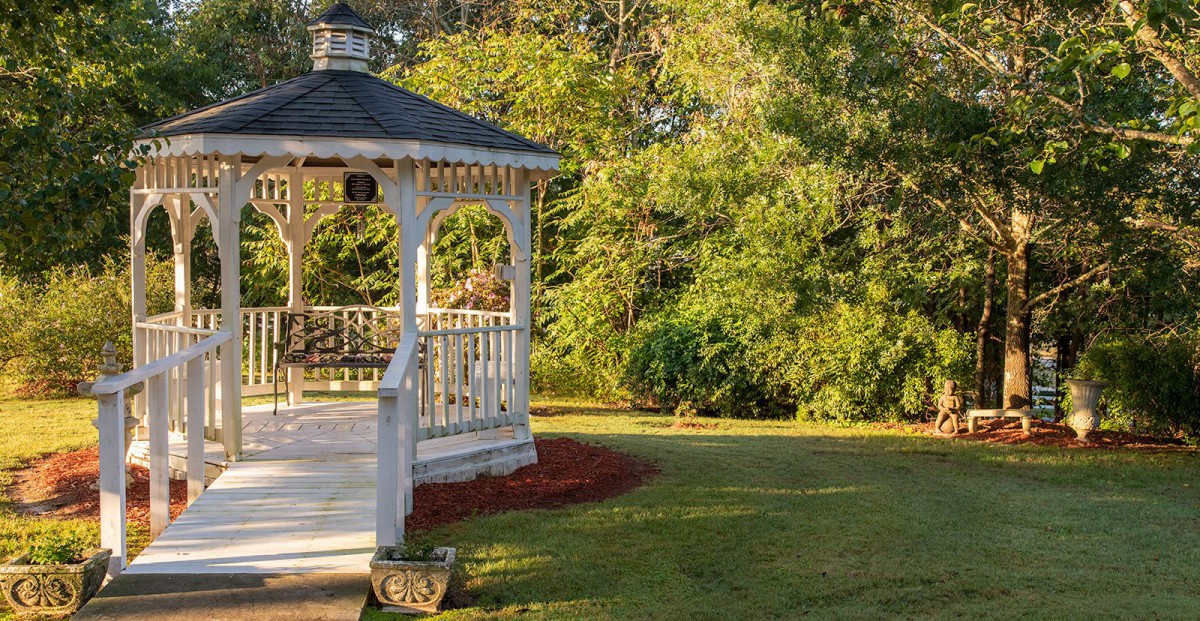 A charming gazebo surrounded by a lush garden and trees in the warm sunlight.