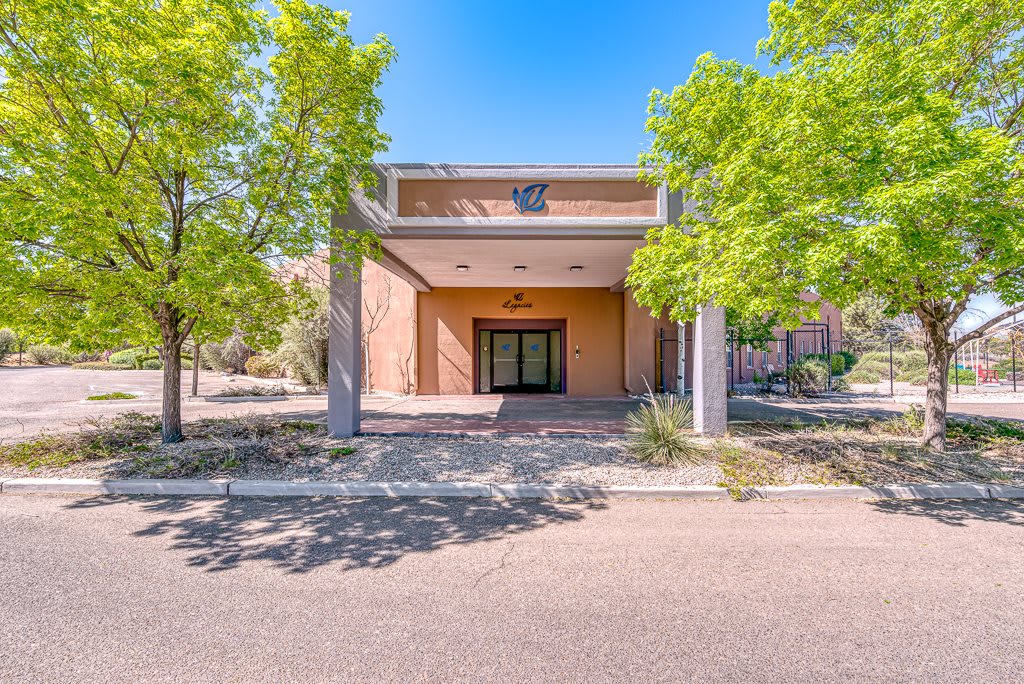 A modern building entrance surrounded by trees on a sunny day.