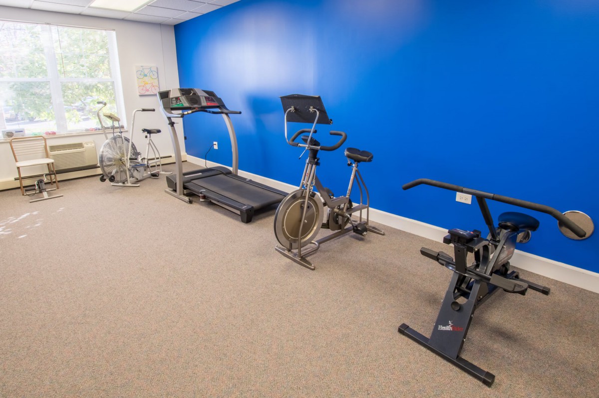 A small gym with exercise equipment including a treadmill and stationary bikes against a blue wall.