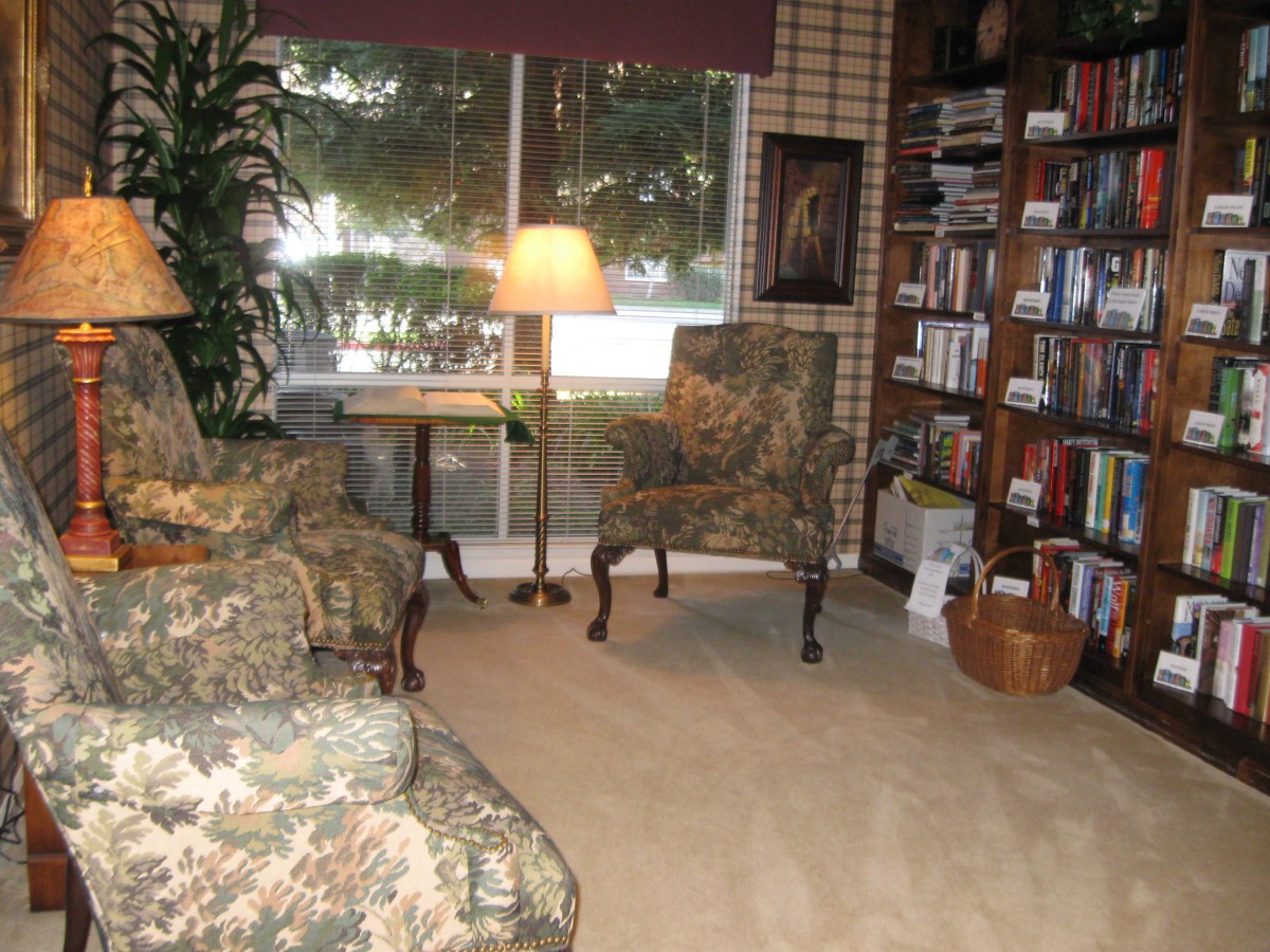 A cozy living room with a bookshelf, armchairs, and a large window bringing in natural light.