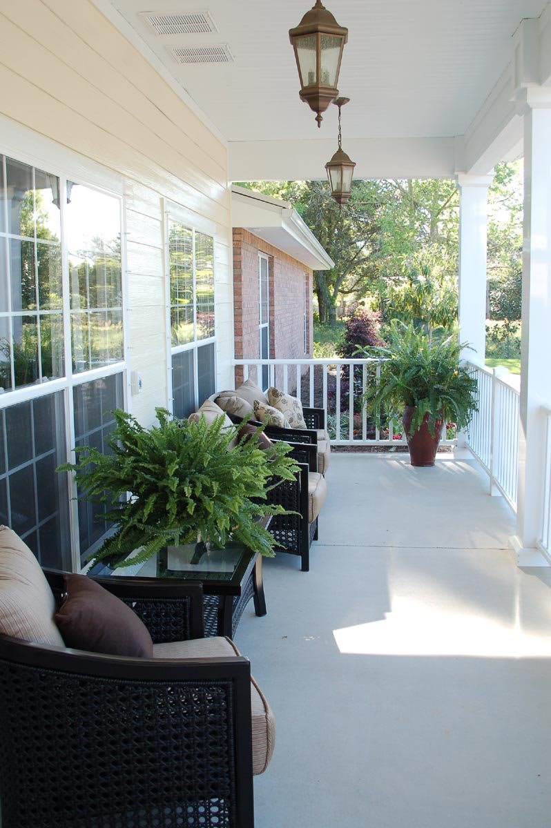 A cozy porch area with outdoor seating and lush plants, bathed in sunlight.