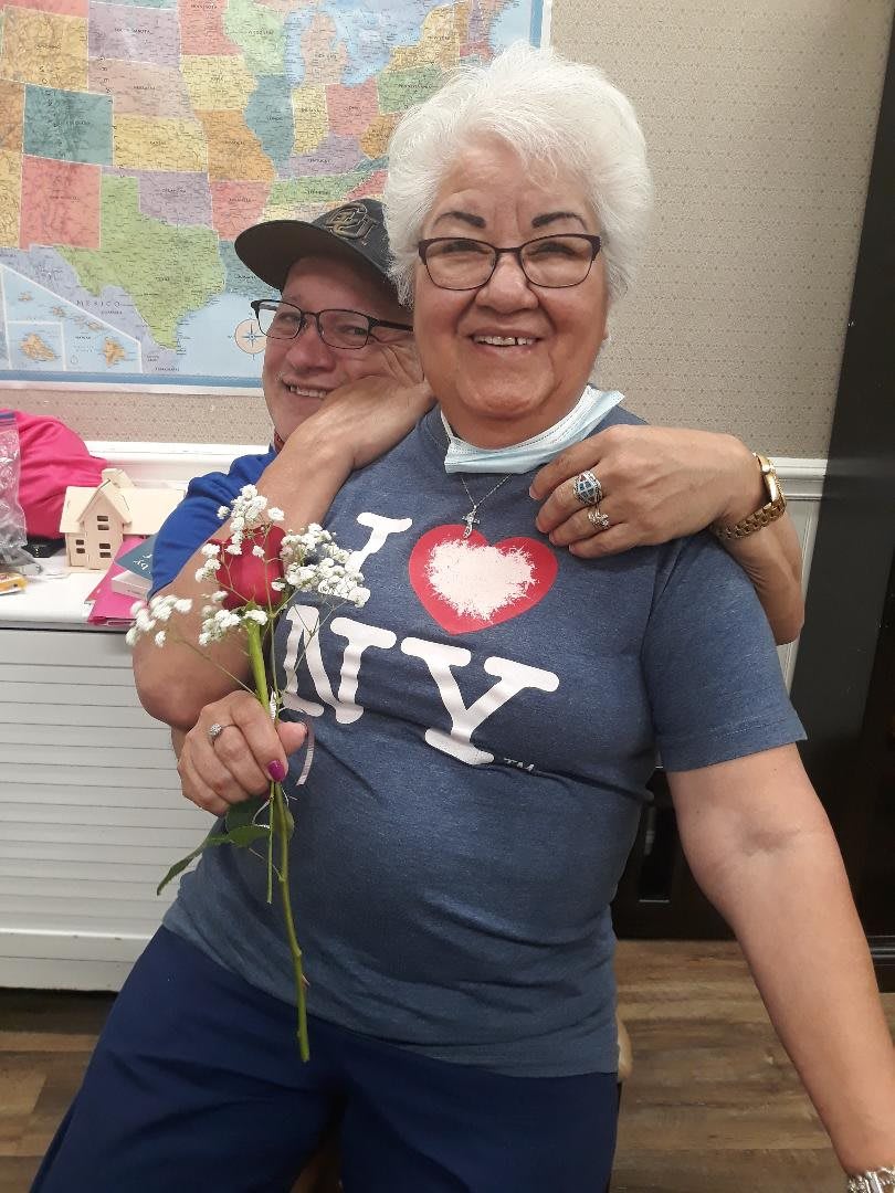 Two people smiling, with one holding a flower and wearing an 'I Love NY' t-shirt.