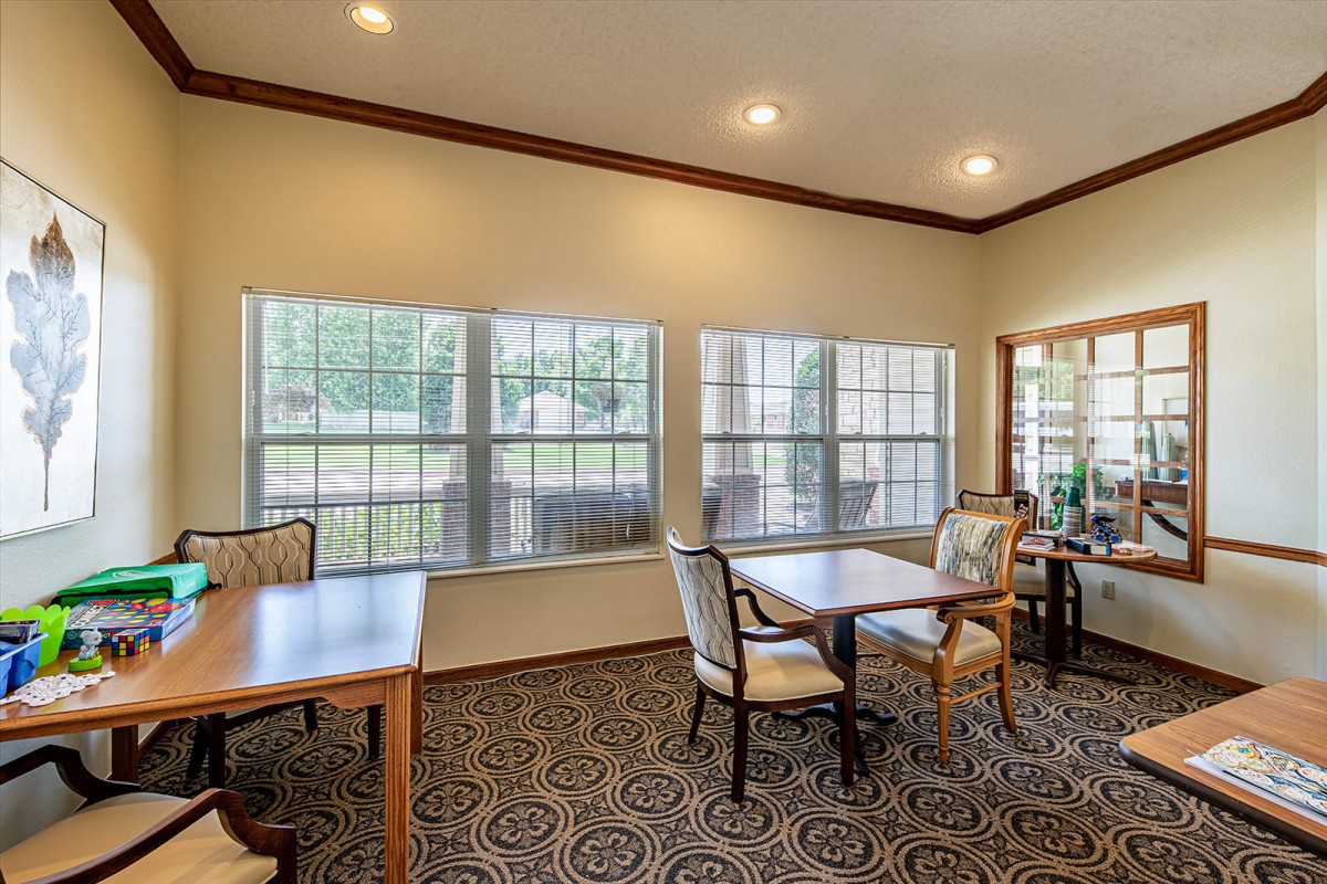 A cozy dining area with tables and chairs, featuring large windows and elegant carpet.