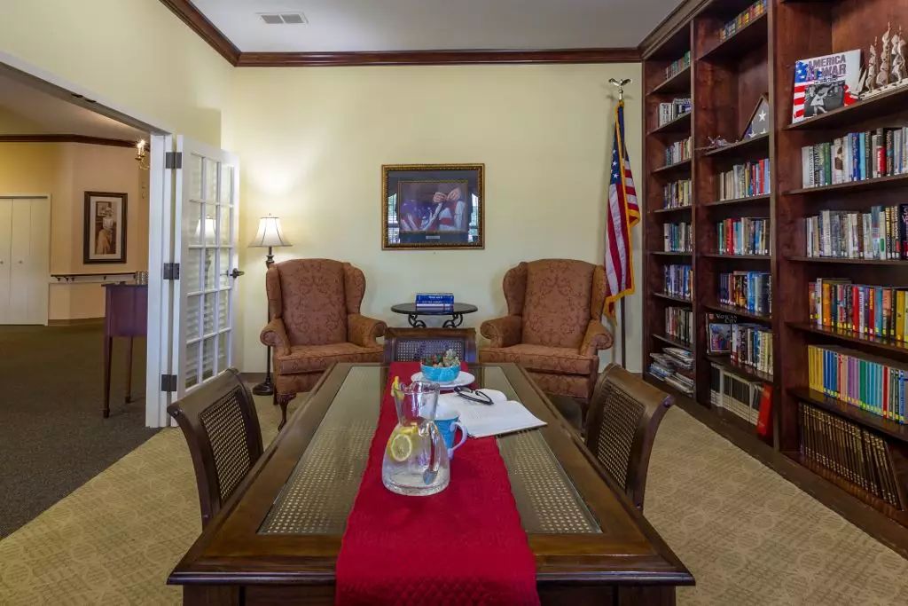A cozy office with bookshelves, armchairs, a table, and an American flag.