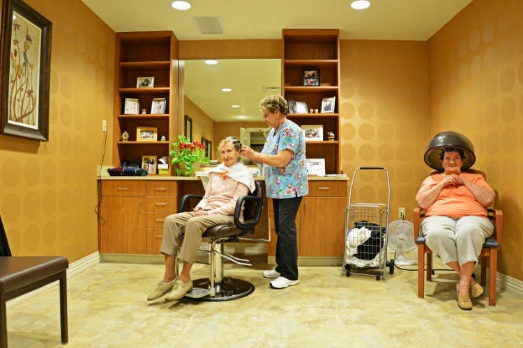 A hairdresser provides a haircut to a senior in a salon setting, emphasizing care and service.