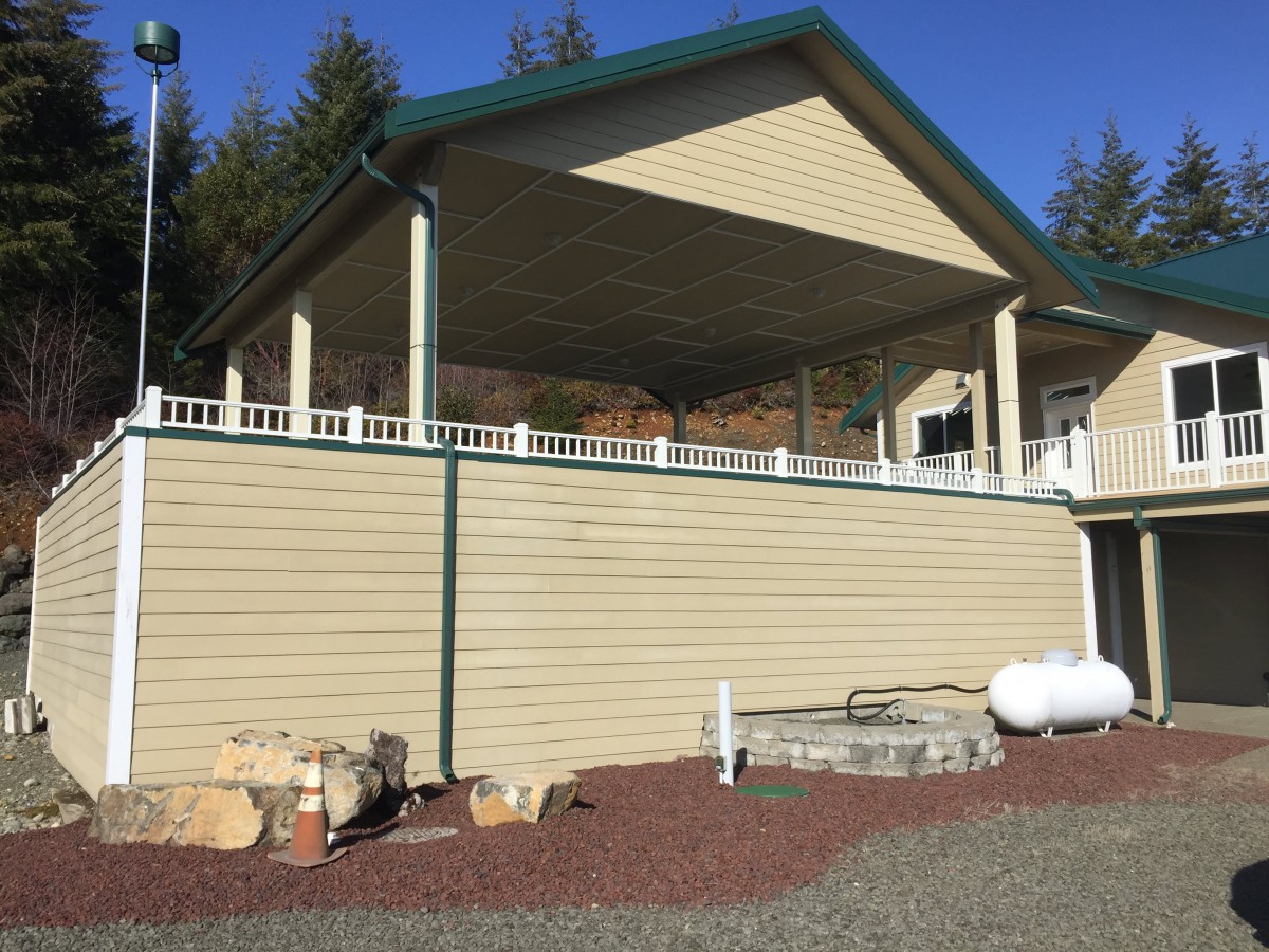 The image features a house with a spacious covered porch and a propane tank in the yard.