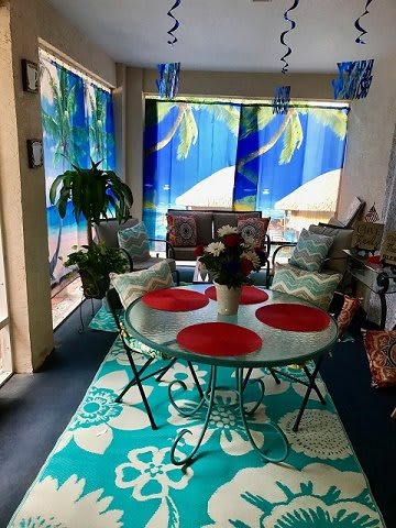A cozy patio area featuring a round dining table with red placemats, surrounded by cushioned chairs and vibrant tropical decor.