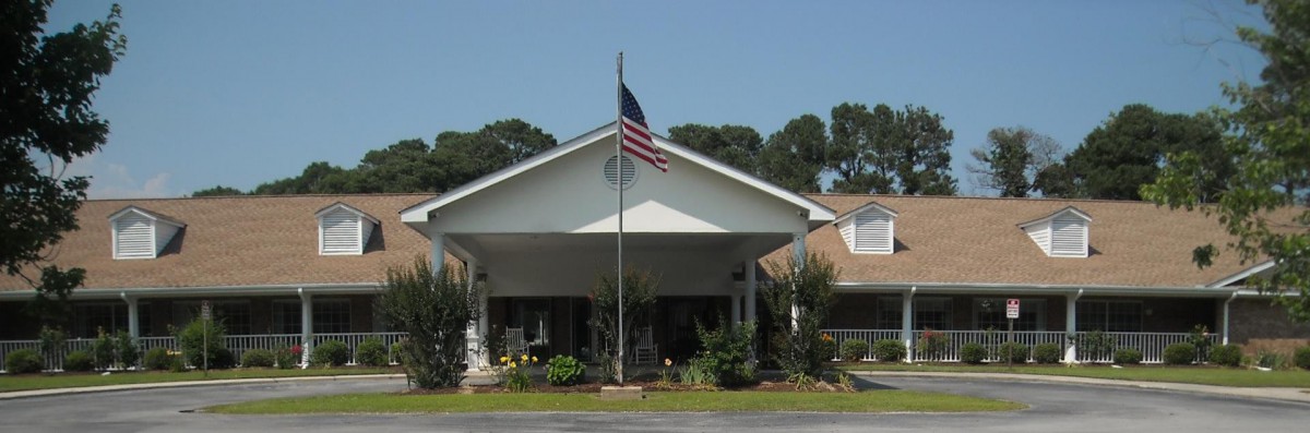 A residential building with an American flag flying, surrounded by a garden and trees.