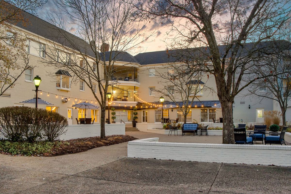 A peaceful courtyard in the evening with ambient lighting and trees surrounding a seating area.