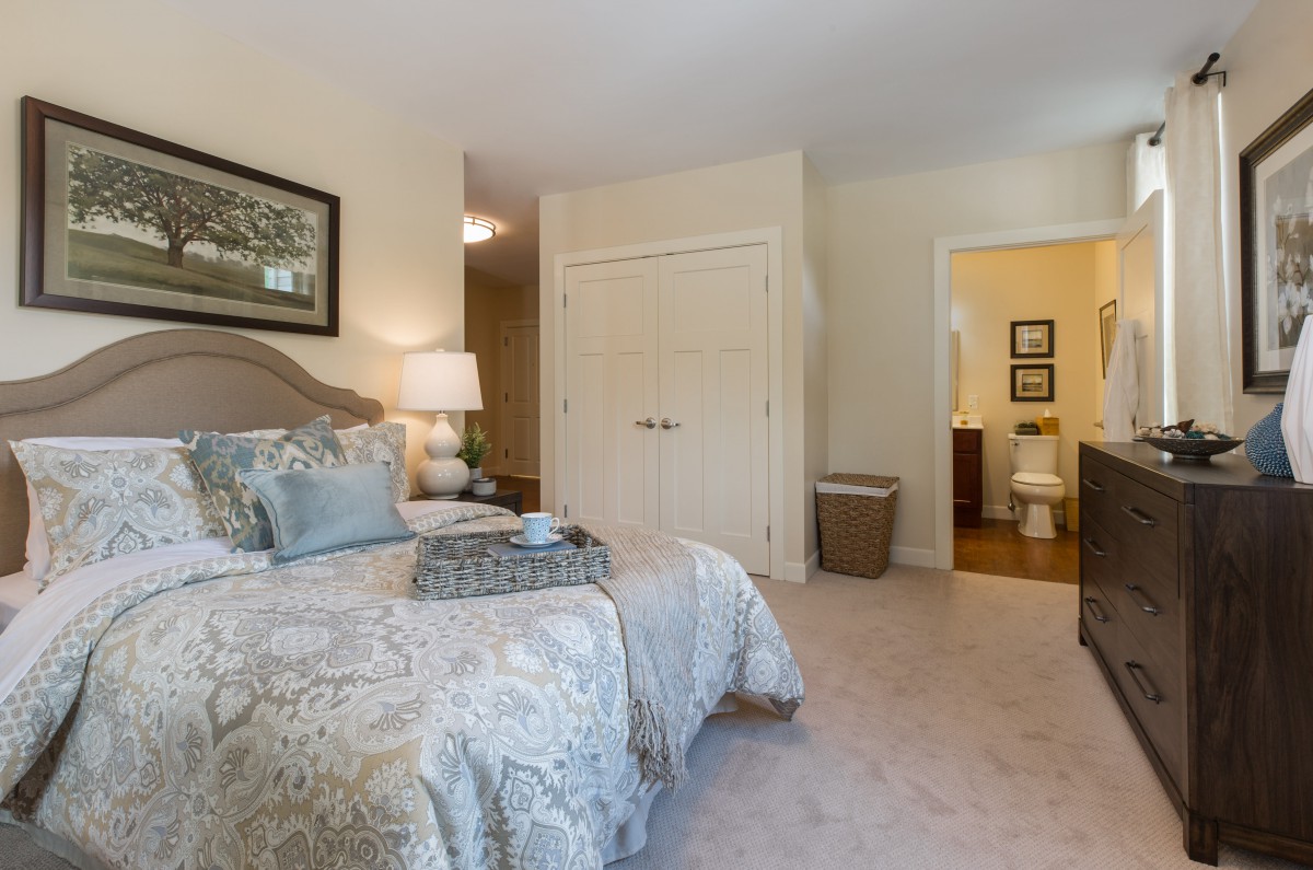 A cozy bedroom with elegant decor featuring a bed, bedside lamp, and an adjacent bathroom.