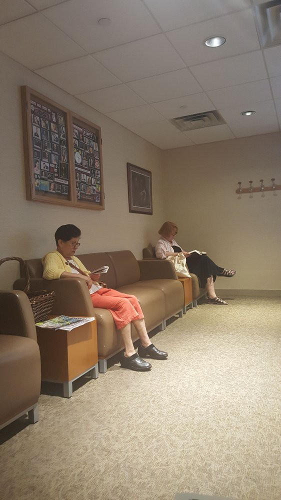 Two people sitting in a waiting room, occupying themselves with reading and using a smartphone.
