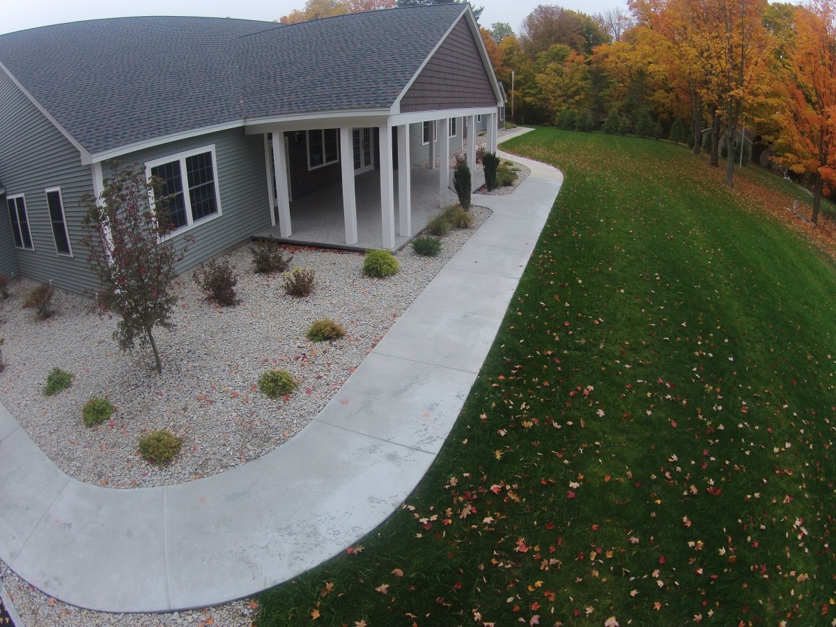 A house with a surrounding sidewalk, neatly landscaped lawn and trees displaying autumn colors.