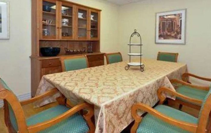 A dining room with a large table covered by a patterned tablecloth, surrounded by wooden chairs and a china cabinet in the background.
