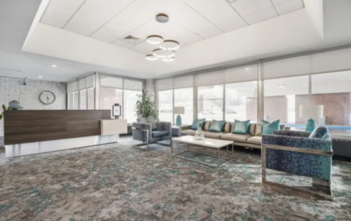 A modern office waiting area with a reception desk, comfortable seating, and large windows providing natural light.