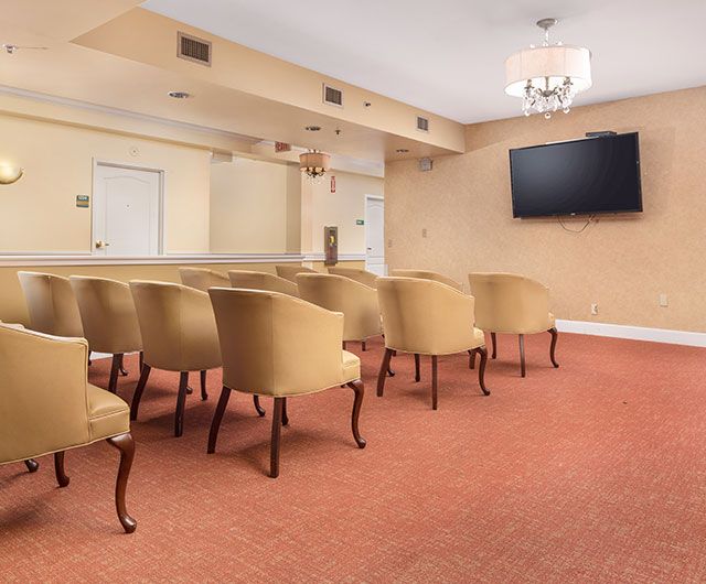 A small conference room with rows of beige chairs facing a wall-mounted television.
