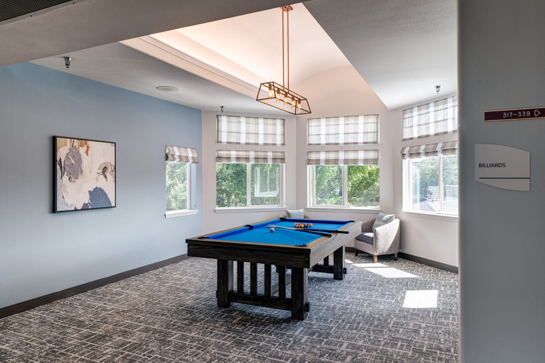 A modern game room featuring a pool table with blue felt under ample natural light.