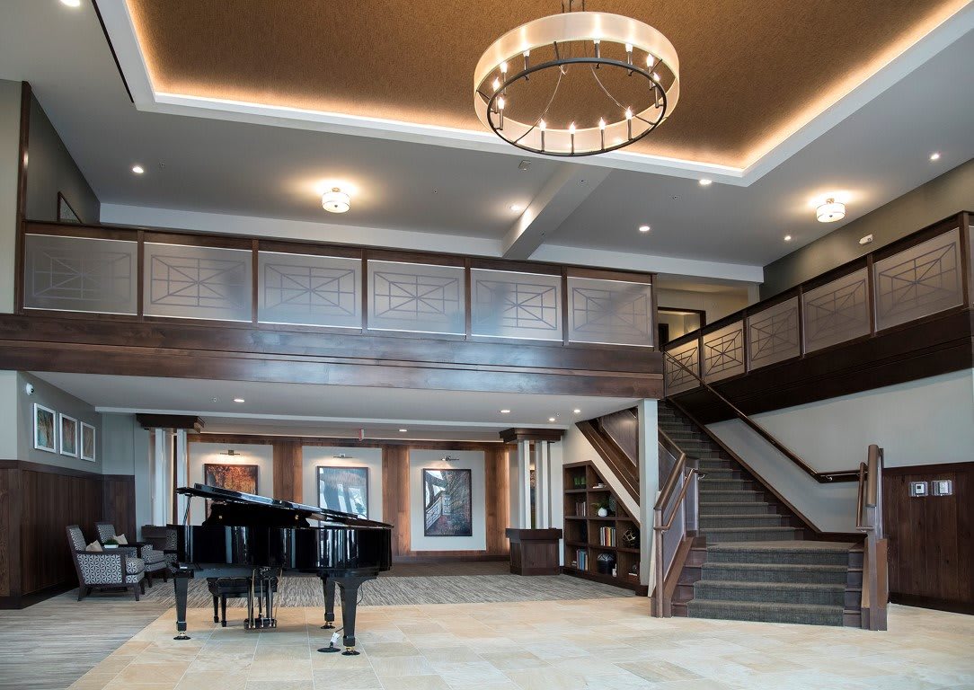 A spacious modern lobby with a grand piano, chandelier, and staircase.