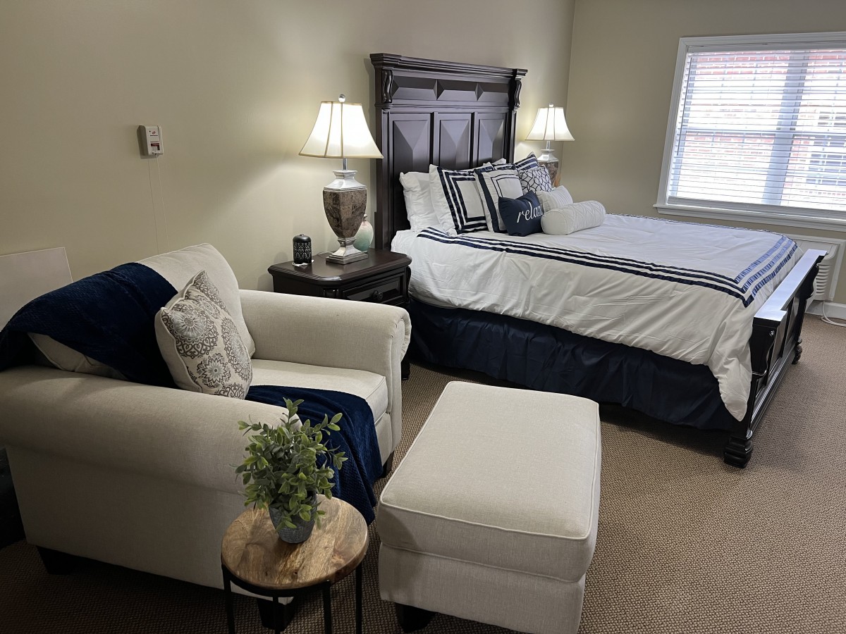 A cozy bedroom with a neatly made bed, a comfortable armchair, and elegant lighting.