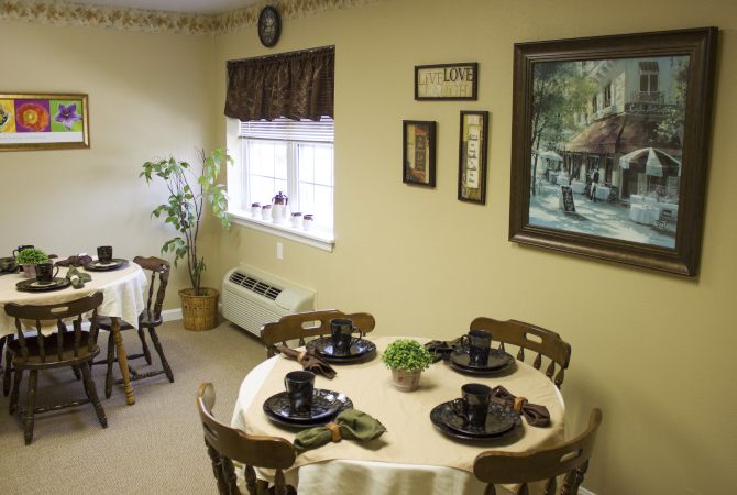 A cozy dining room with a round table set for four, decorated with paintings and plants.