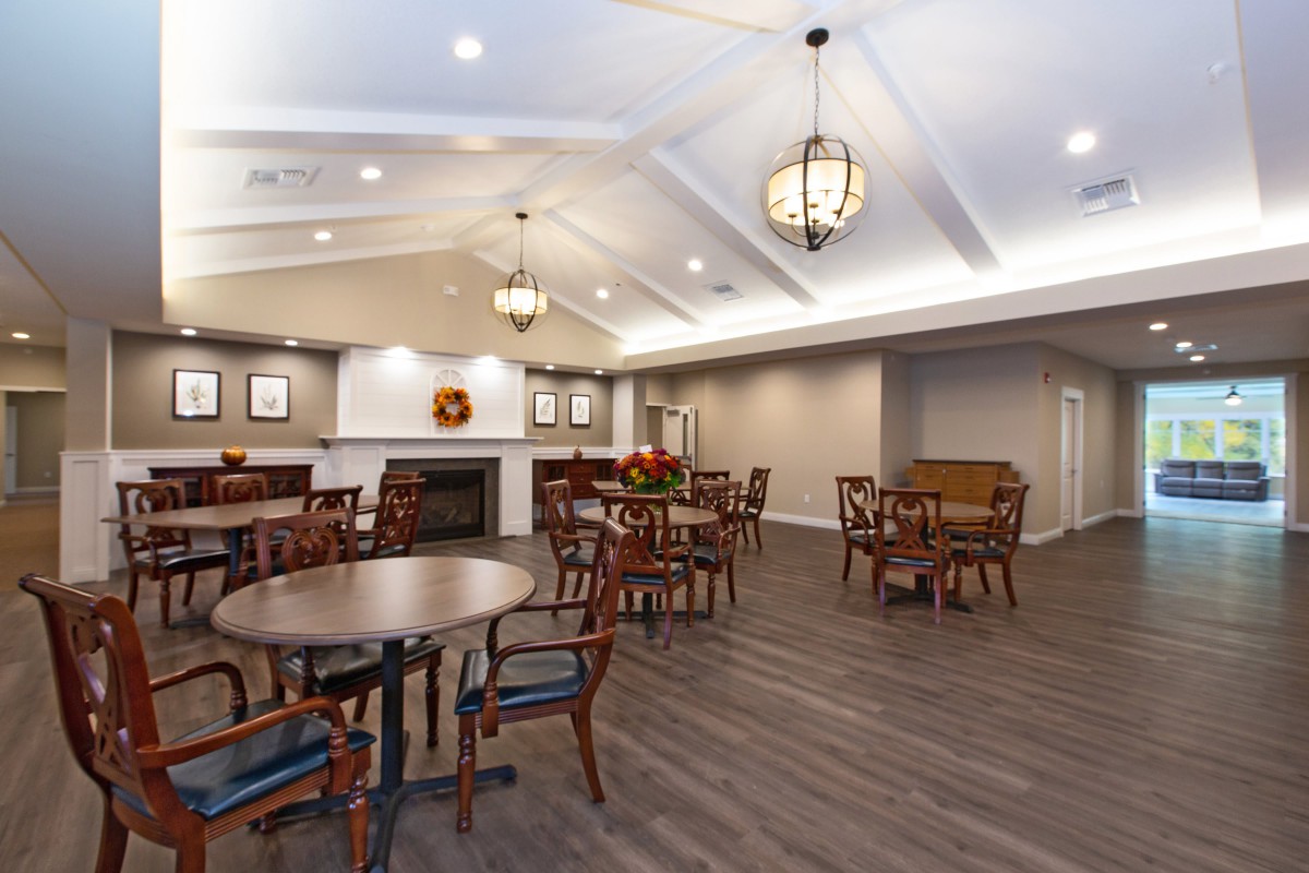 A spacious dining area featuring multiple tables and chairs, with elegant lighting and a wooden floor.