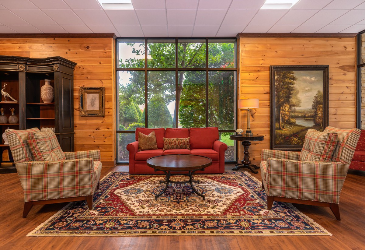 A cozy living room with wood paneling, featuring a red sofa, armchairs, and a decorative rug.