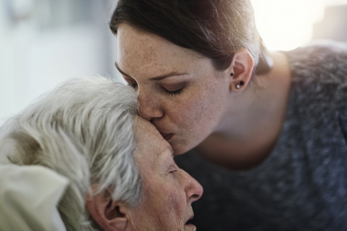 A woman tenderly kisses the forehead of an elderly person, expressing love and care.