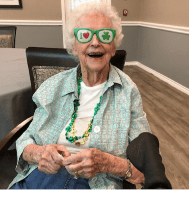 An elderly woman smiling while wearing fun glasses indoors.