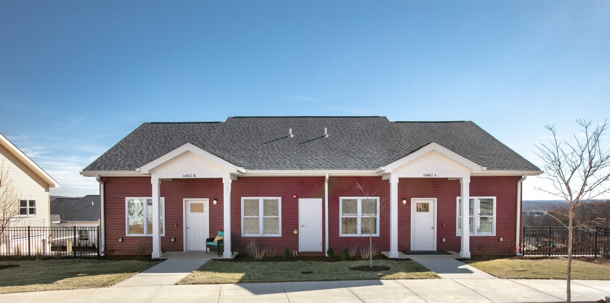 A red duplex with white trim under a clear blue sky.