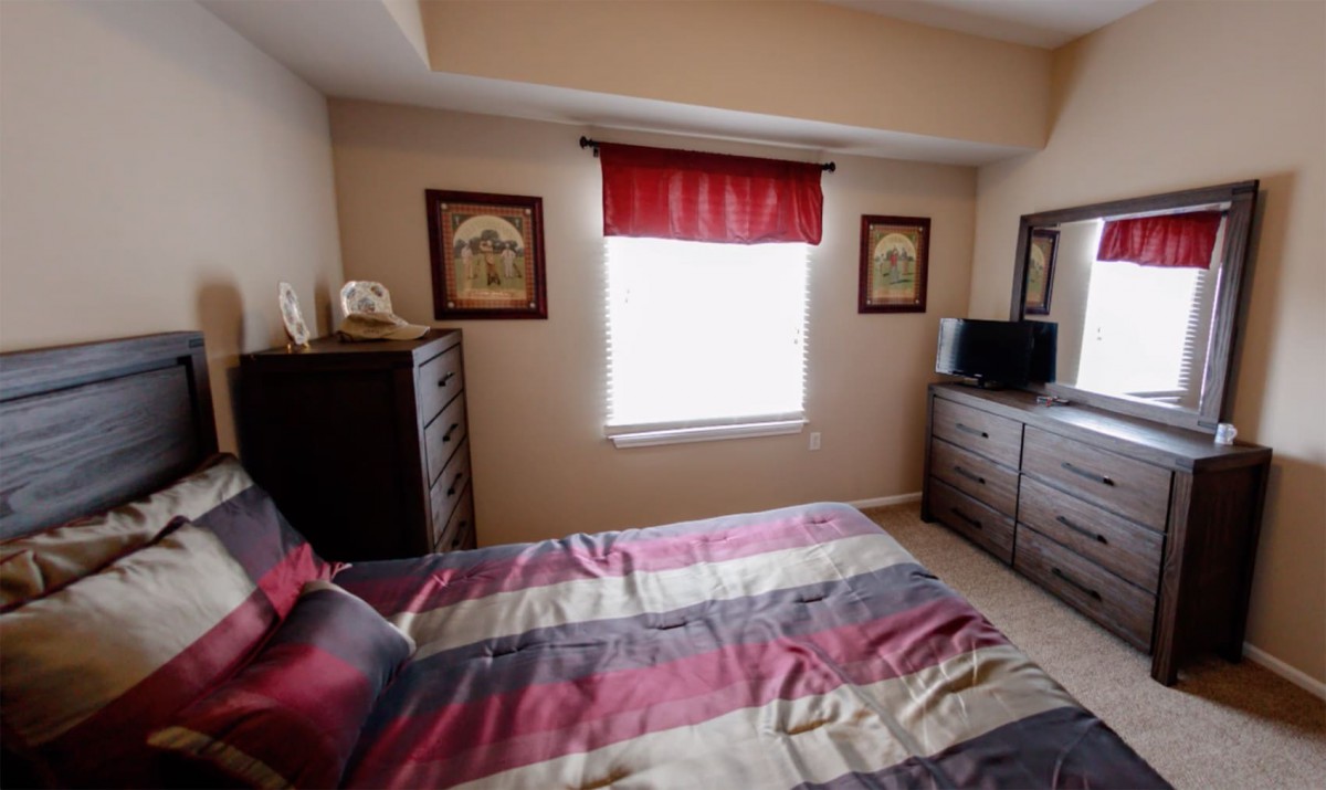 Cozy bedroom with a striped bedspread, dresser, and a small TV under a window with red valance.
