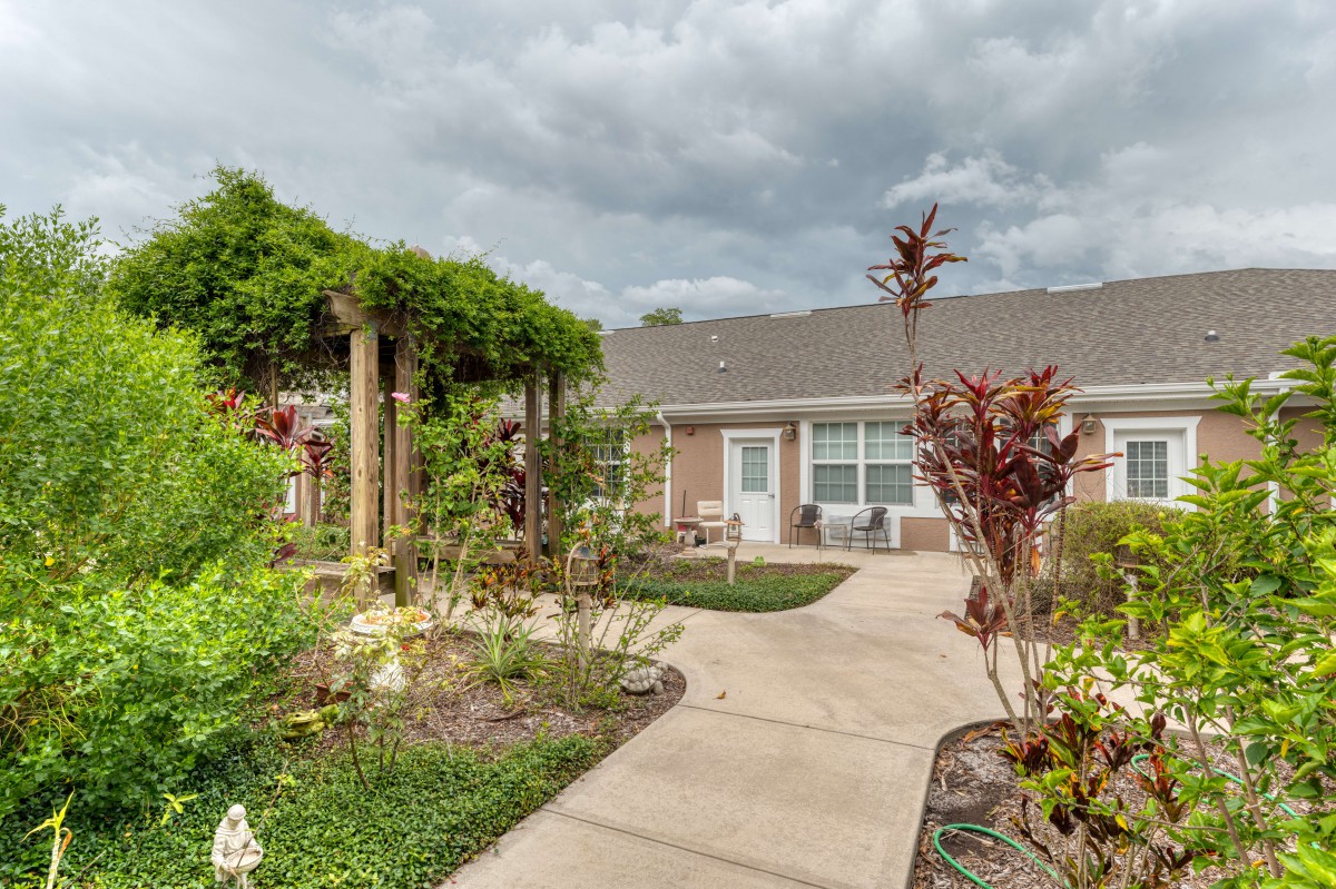 A beautiful garden with a pathway leading to a house under cloudy skies.
