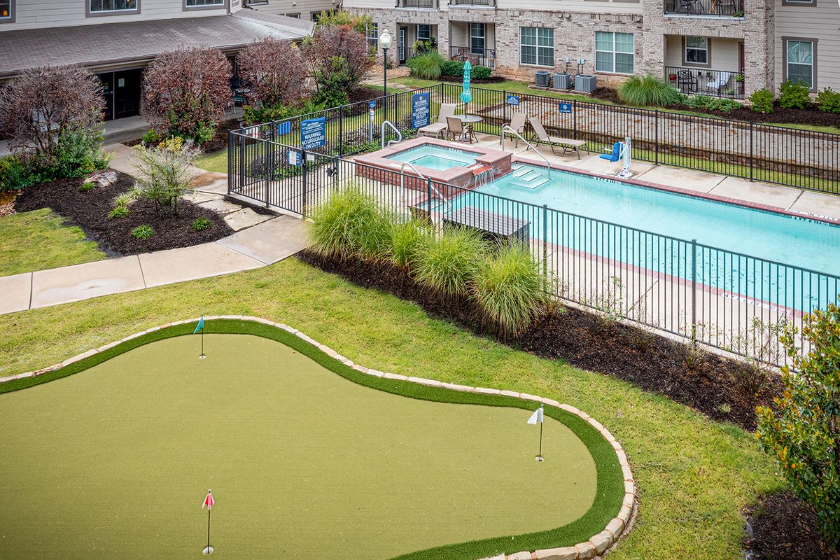 A view of a modern apartment complex featuring a putting green and a swimming pool surrounded by landscaped gardens.