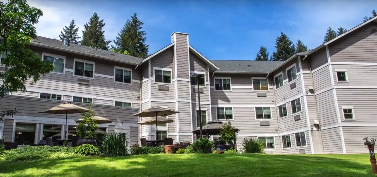 A multi-story residential building surrounded by trees and a grassy area under a clear blue sky.