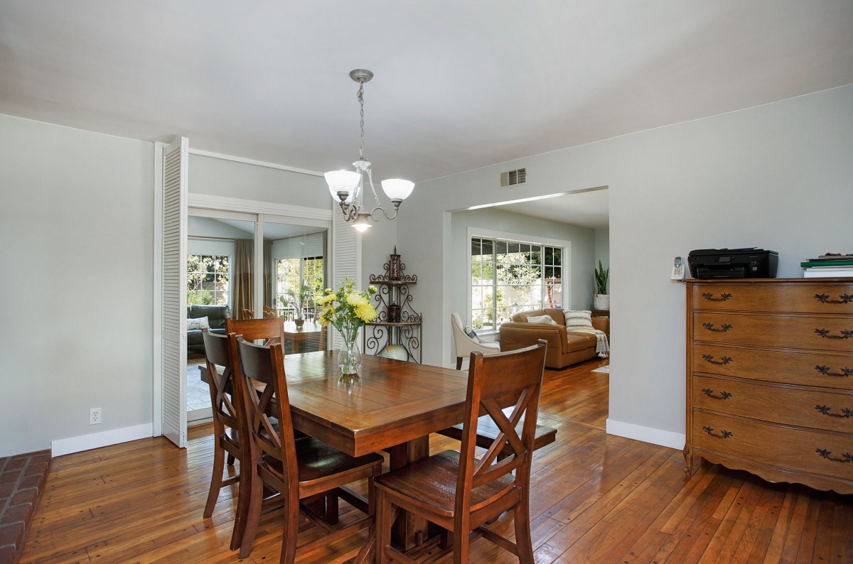 A spacious dining room with a wooden table and chairs, illuminated by a chandelier, featuring hardwood floors and an open concept layout.