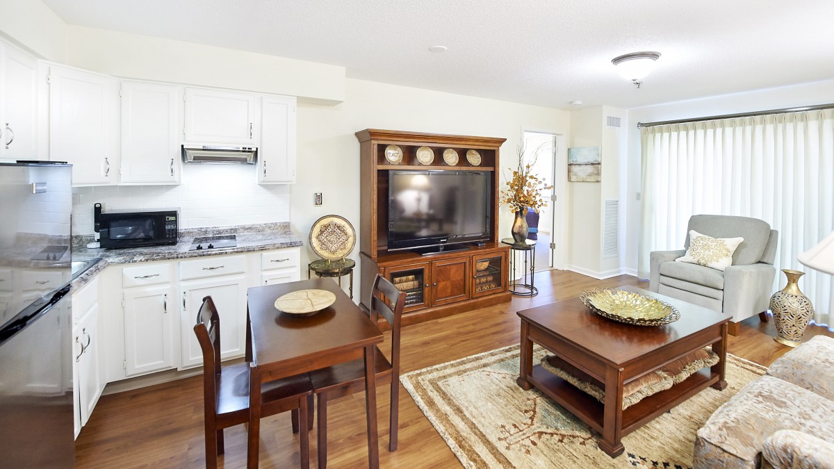 A cozy open-concept living area featuring a dining table, large TV on a wooden stand, and kitchen space.