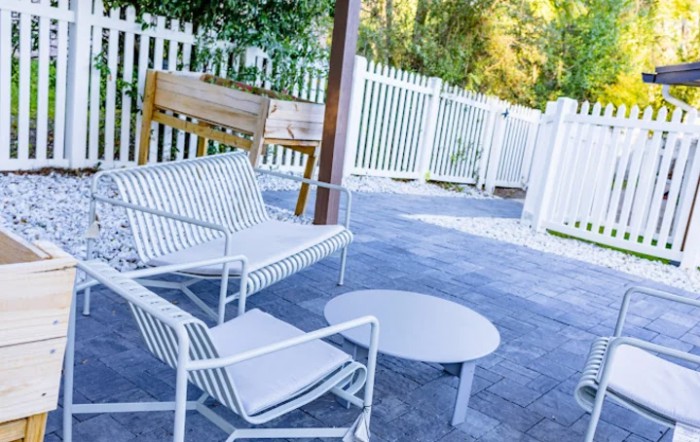A cozy outdoor patio setup with white furniture and a wooden bench against a fenced backdrop.